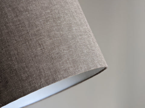 Close-up of a textured fabric lamp shade with a herringbone pattern on a neutral background