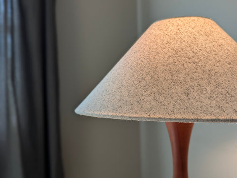 A freckled cotton lamp shade in an extreme tapered shape called a coolie shade on a vintage, teak wood lamp