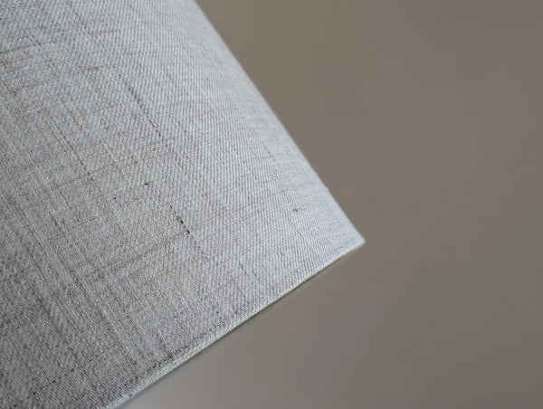 Close-up of a tan and gray linen lamp shade with brass hardware against a blurred background