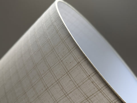 close up of the top of a lamp shade in windowpane grid fabric against a neutral background