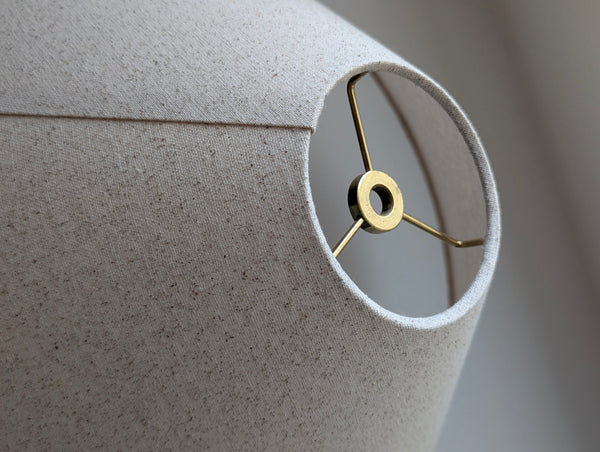 Close-up of a textured lampshade with a brass fitting on a neutral background