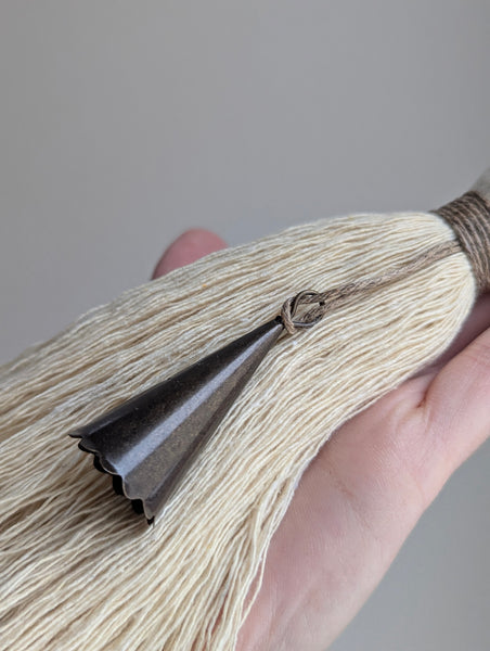 Close-up of a hand holding a decorative tassel with a plain background