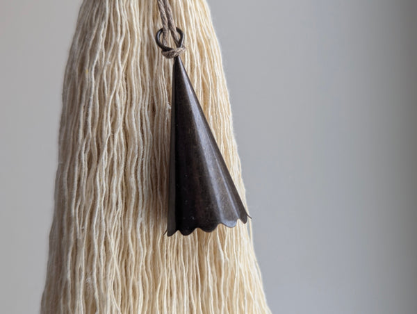 Black triangular bell hanging from a tassel on a textured beige background
