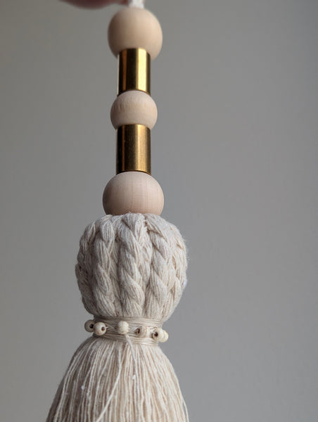 Decorative tassel with wooden beads and a brass accent on a gray background