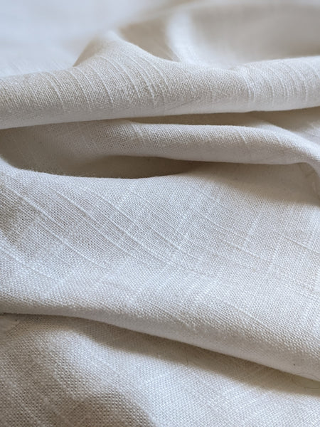A close-up of draped off-white fabric with a subtle woven texture and soft folds.
