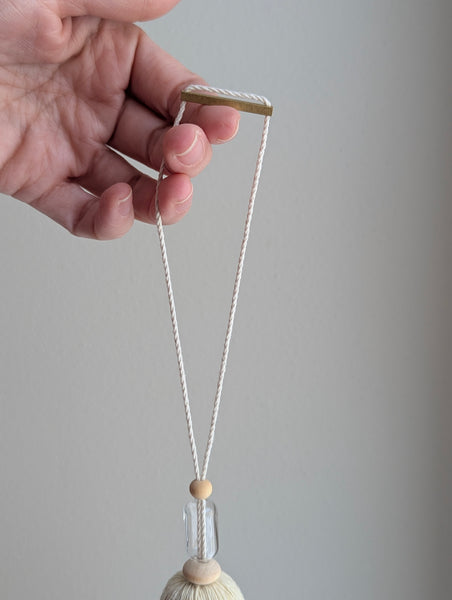 Decorative tassel with wooden and glass beads and a brass bar on a gray background