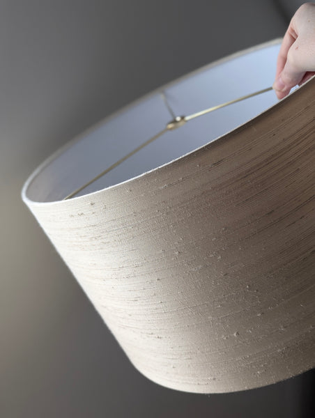 Close-up of a hand holding a beige lampshade against a dark background