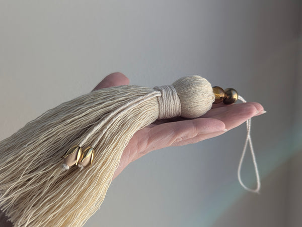 Hand holding a decorative tassel with a plain background