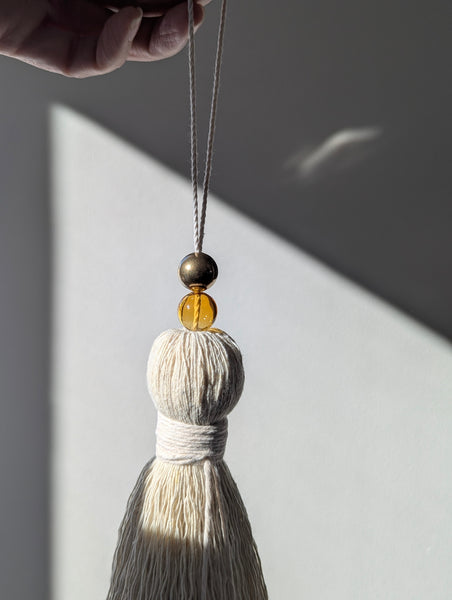 Tassel with a amber glass bead and a brass bead against a neutral background