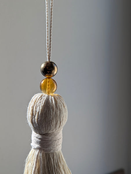 Tassel with two round beads on a string against a gray background