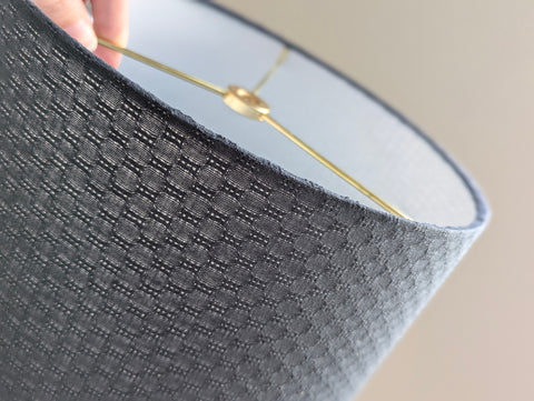 anthracite lace lamp shade with brass hardware being held by a hand