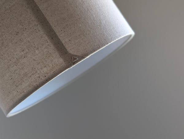 Speckled Oatmeal cotton fabric lampshade with brass hardware against a blurred background