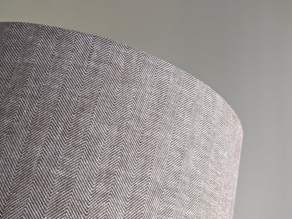 Close-up of a textured fabric lamp shade with a brown herringbone pattern on a neutral background
