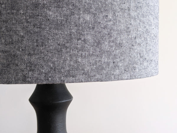 back and white woven fabric lampshade on a black table lamp against a neutral background