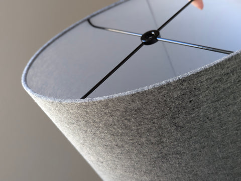 front side of an oval lamp shade with grey fabric and black spider ring hardware