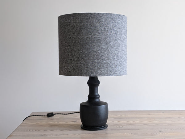 textured gray lamp shade on a black table lamp on a light wood table