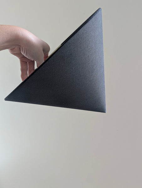 A hand holding a black linen cone lamp shade against a plain light beige background.