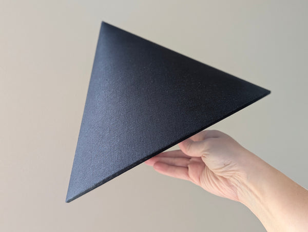 A hand holding a black linen cone lamp shade against a plain light beige background.