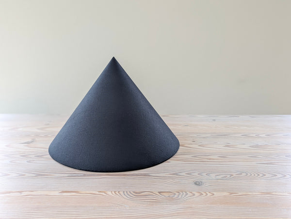 A black linen cone lamp shade sitting on a light wood table against a plain light beige background.