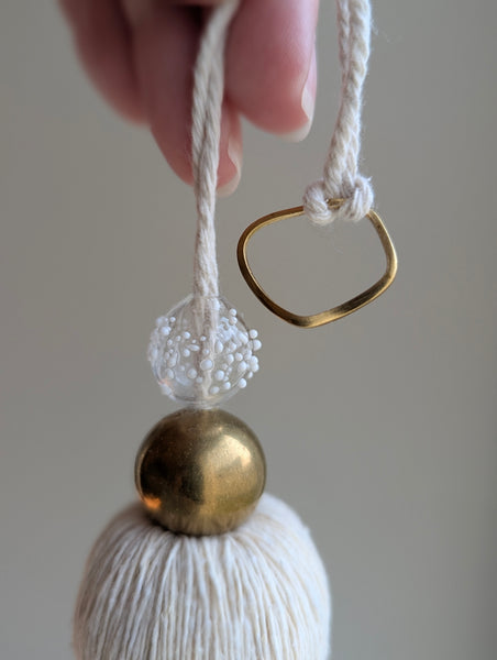 snowy white tassel in a natural cotton color with brass accents and a handblown glass bead