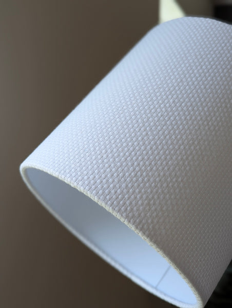 Close-up of a white textured lampshade in Bright White Crosshatch fabric against a soft gray background