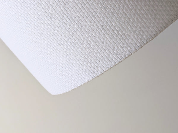 Close-up of a white textured lampshade in Bright White Crosshatch fabric against a soft gray background