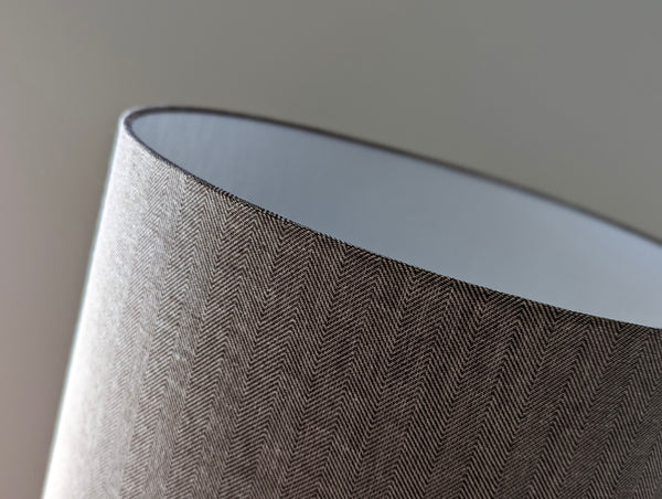 Close-up of a textured fabric lamp shade with a brown herringbone pattern on a neutral background