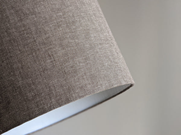 Close-up of a textured fabric lamp shade with a herringbone pattern on a neutral background