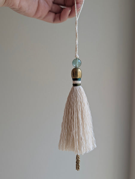 a small festive door tassel made of cotton with a green glass bead and brass accents