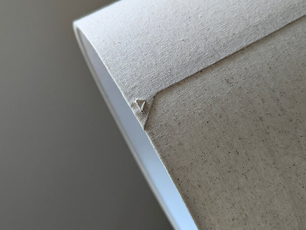 Speckled Oatmeal cotton fabric lampshade with brass hardware against a blurred background