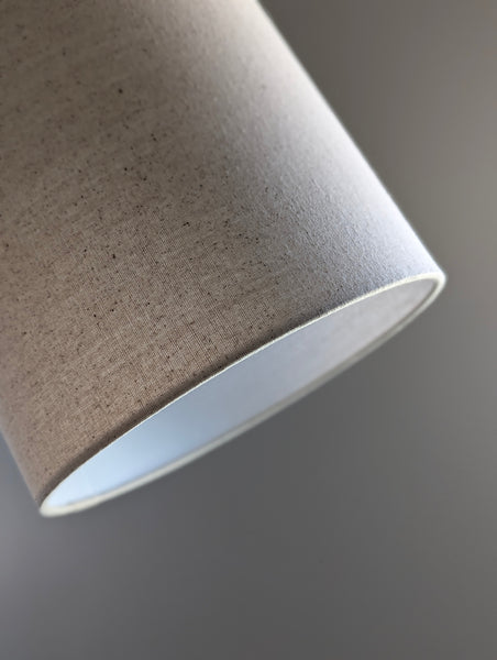 Speckled Oatmeal cotton fabric lampshade with brass hardware against a blurred background