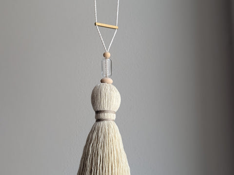 Decorative tassel with wooden and glass beads and a brass bar on a gray background