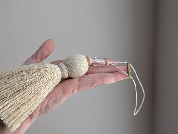 Decorative tassel with wooden and glass beads and a brass bar on a gray background