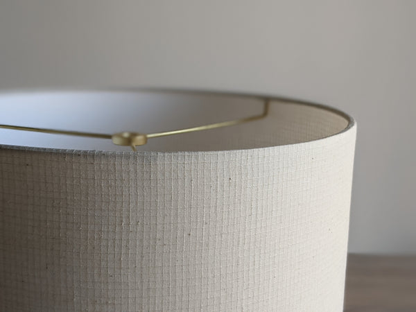 Close-up of a drum lampshade made of textured off-white fabric, with a brass spider washer visible along the top edge.