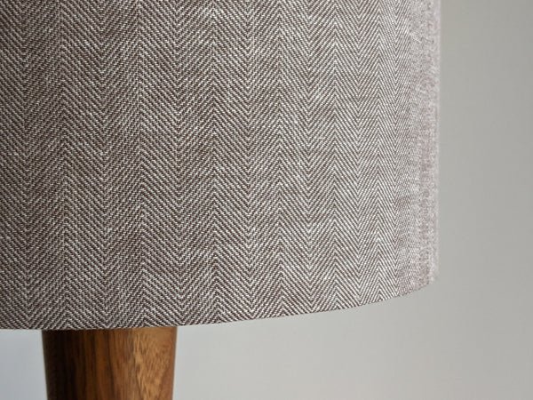 Close-up of a textured fabric lamp shade with a herringbone pattern on a wooden table lamp