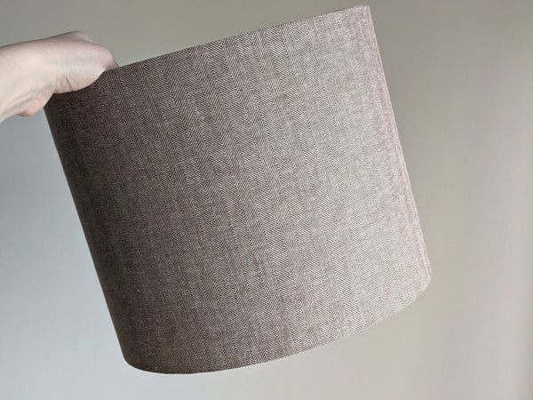 Brown herringbone fabric lamp shade being held by a hand