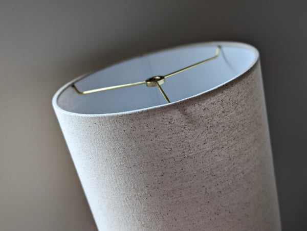 Speckled Oatmeal cotton fabric lampshade with brass hardware against a blurred background
