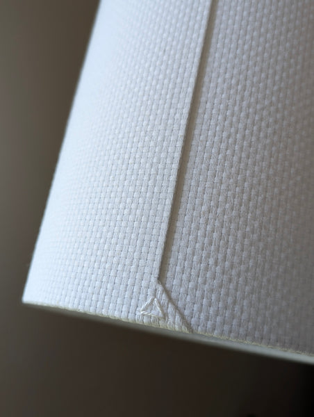 Close-up of a white textured lampshade in Bright White Crosshatch fabric against a soft gray background
