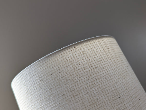 Close-up of a drum lampshade made of textured off-white woven fabric, showing a fine grid pattern