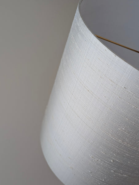 Close-up of a gray silk lampshade with a nubby texture, showing brass hardware inside.