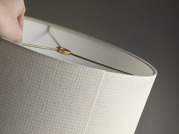 Close-up of a light beige textured fabric lampshade with a brass metal spider washer 