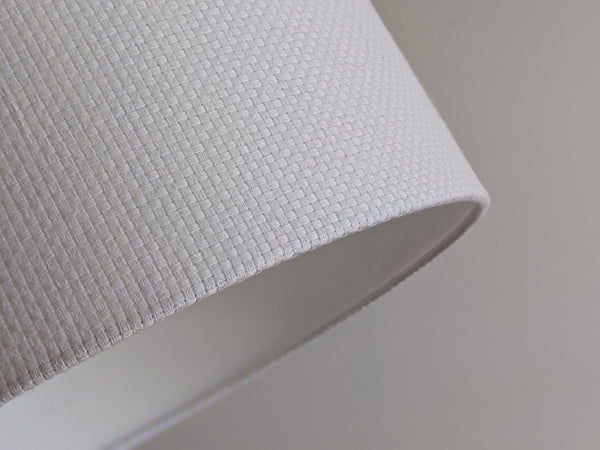 Close-up of a white textured lampshade in Bright White Crosshatch fabric against a soft gray background