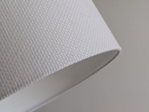 Close-up of a white textured lampshade in Bright White Crosshatch fabric against a soft gray background