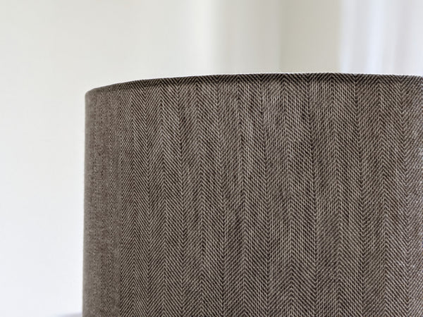 Close-up of a textured fabric lamp shade with a brown herringbone pattern on a neutral background