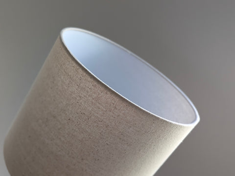 Speckled Oatmeal cotton fabric lampshade with brass hardware against a blurred background