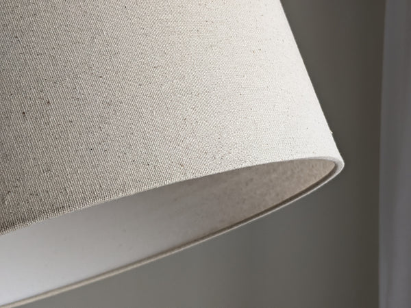 Speckled Oatmeal cotton fabric lampshade with brass hardware against a blurred background