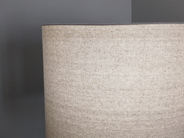 Speckled Oatmeal cotton fabric lampshade with brass hardware against a blurred background