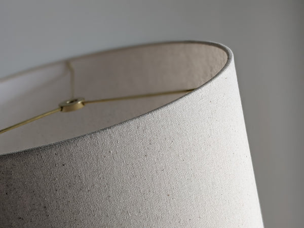 Speckled Oatmeal cotton fabric lampshade with brass hardware against a blurred background