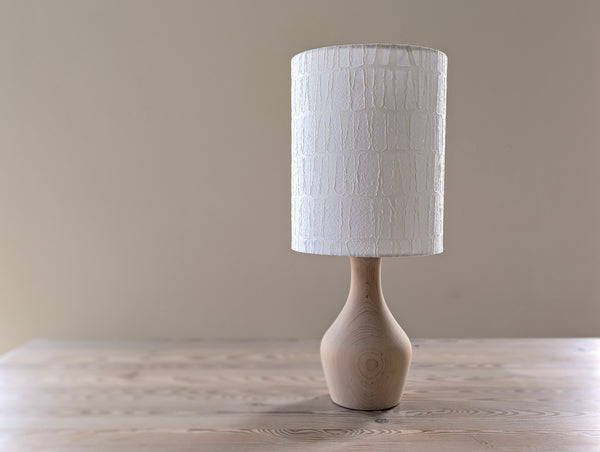 light wood table lamp with textured white lamp shade on a wooden table