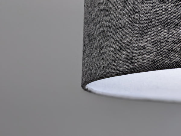 Close-up of a textured gray lampshade with light shining through it on a plain background